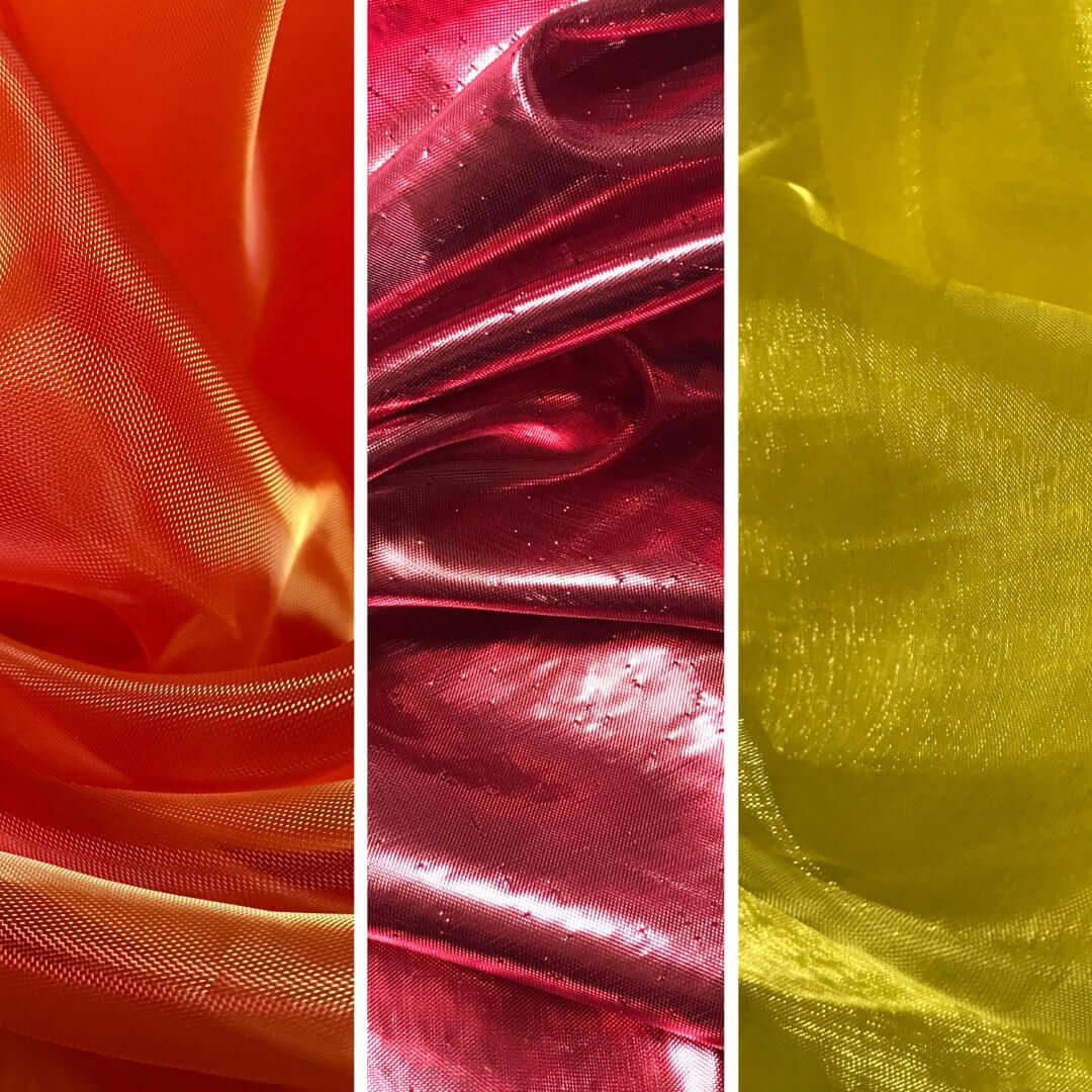 A side-by-side comparison of sheer, shimmery fabrics in three bold colors. From left to right: fiery orange with golden undertones, deep scarlet red with a subtle sparkle, and bright, luminous yellow. The fabrics have a flowing texture and iridescent finish, ideal for worship flags or expressive dance.