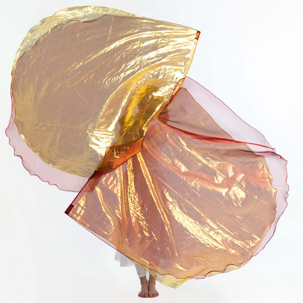 Worship flags in radiant bronze and gold shimmer fill the frame, gracefully fanned out in motion, with only the bare feet of the dancer visible beneath the flowing fabric.