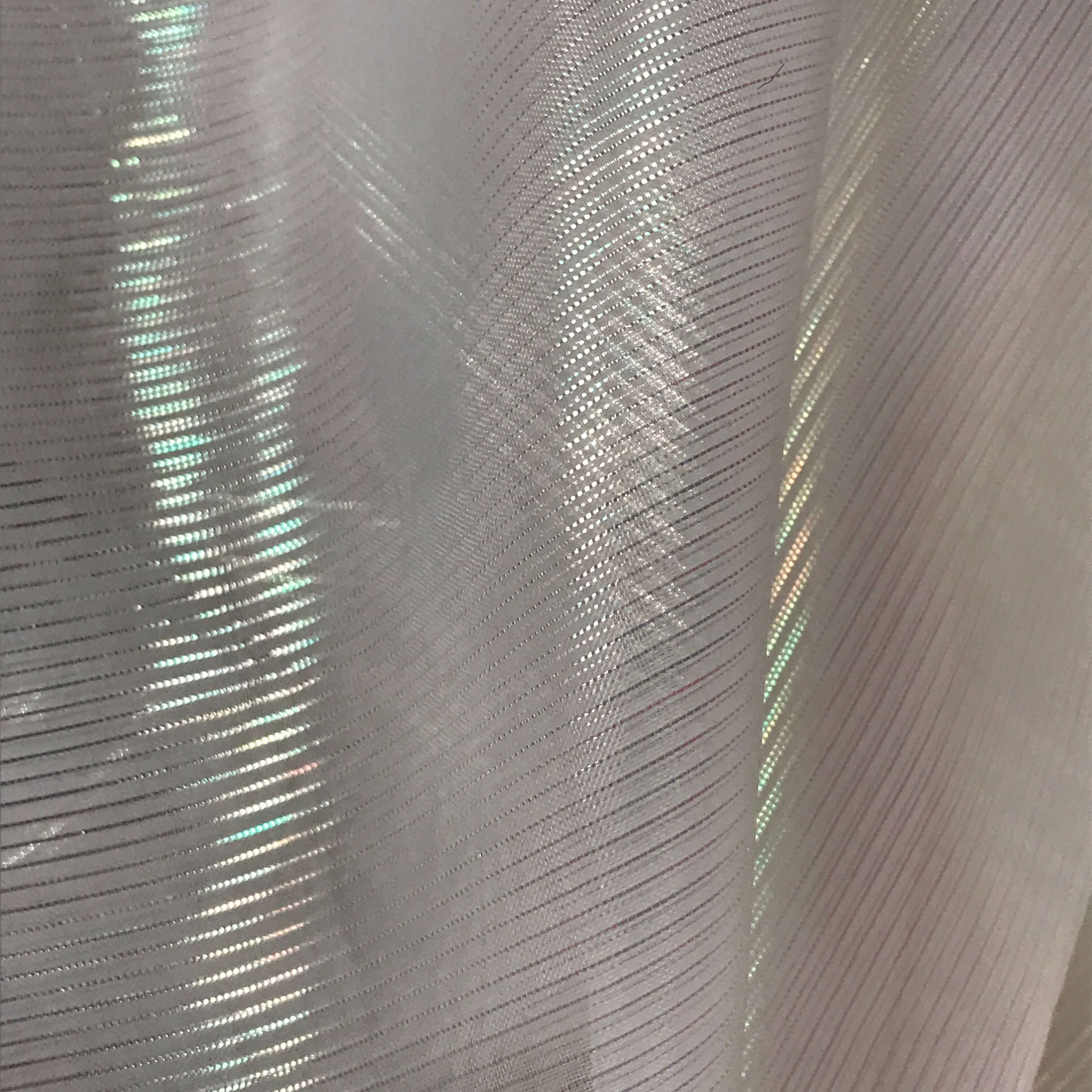 "Close-up of sheer iridescent crystal fabric with diagonal textured lines and subtle rainbow reflections, catching light in a delicate shimmer.