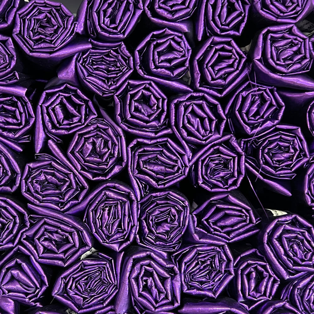 Rolled purple metallic fabric stacked in a display, ideal for DIY worship flags. Symbolizes royalty, intercession, and consecrated praise in biblical worship.