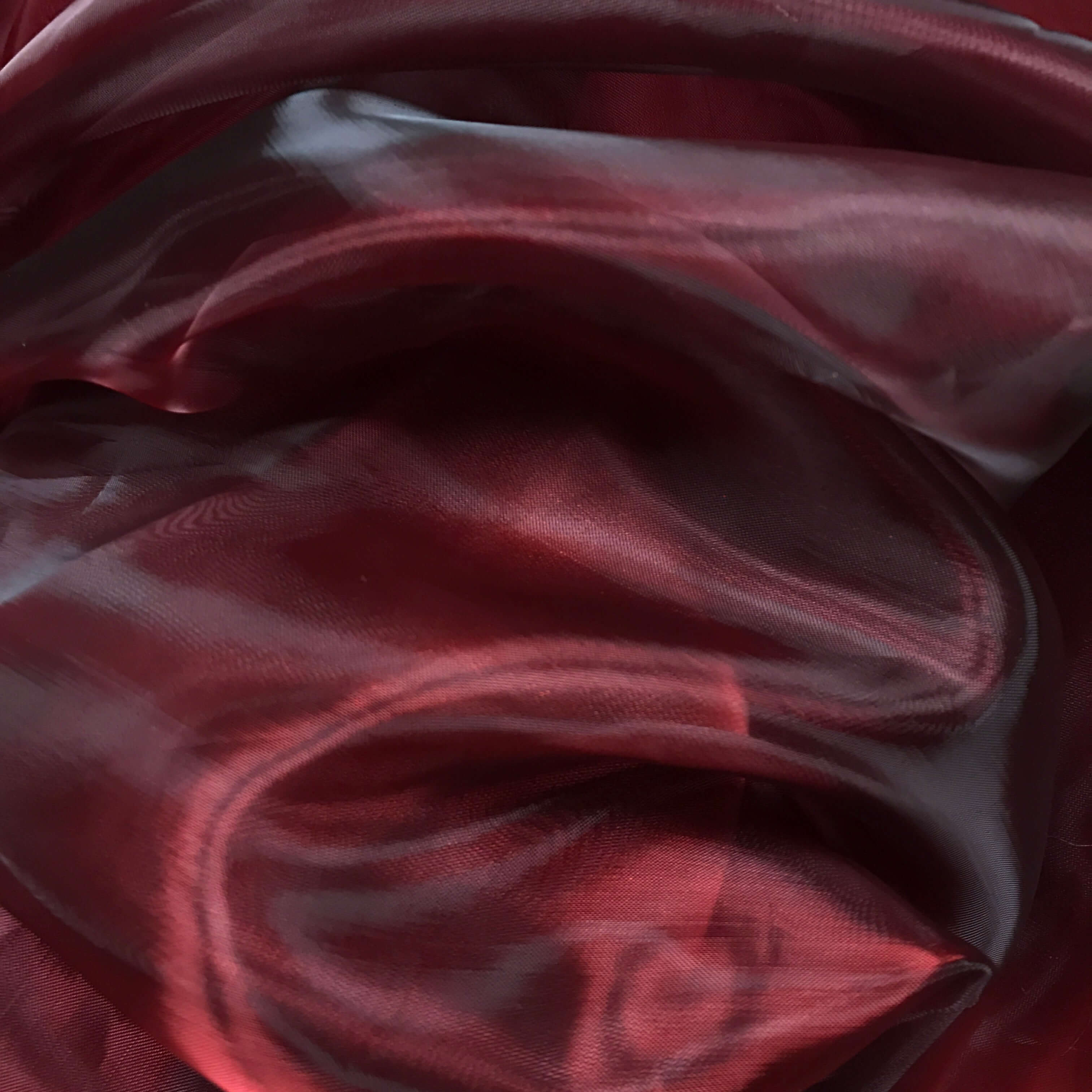 Close-up of flowing wine-colored iridescent fabric with deep red and burgundy tones, capturing elegant light reflections ideal for worship flags or dance garments.