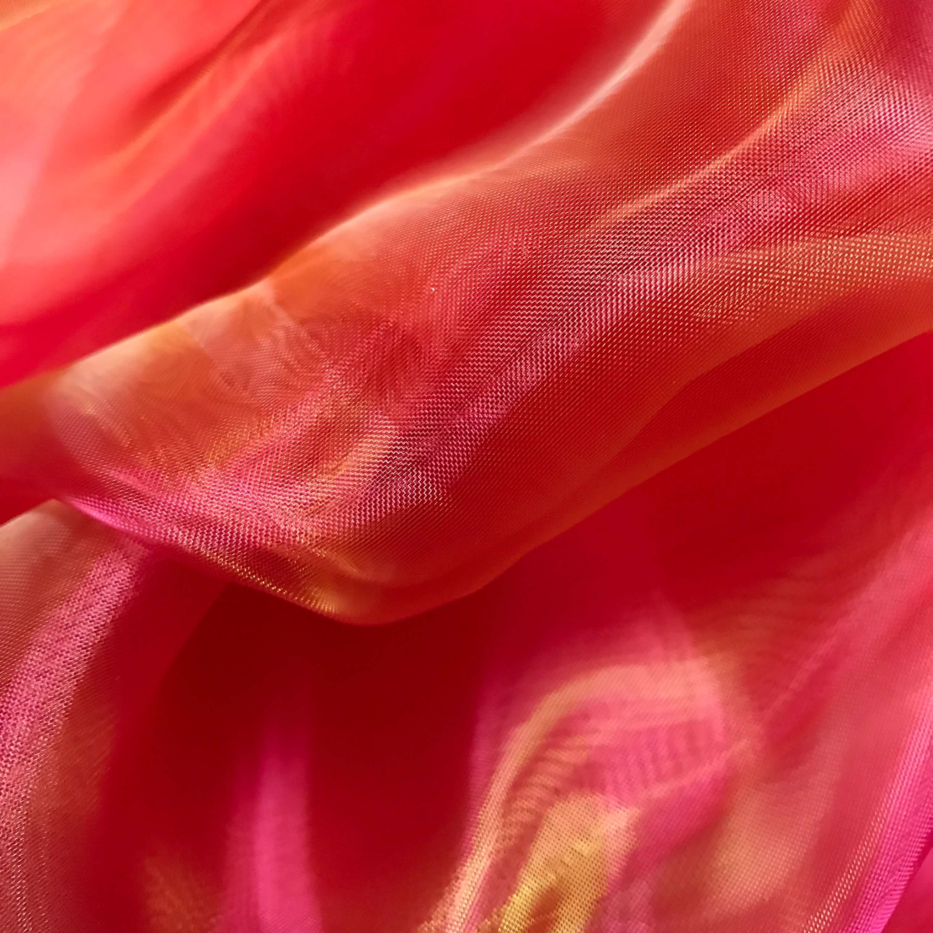 Close-up of flowing pink and coral sheer fabric with hints of orange and yellow shimmer, highlighting the iridescent texture ideal for worship flags or dance garments.