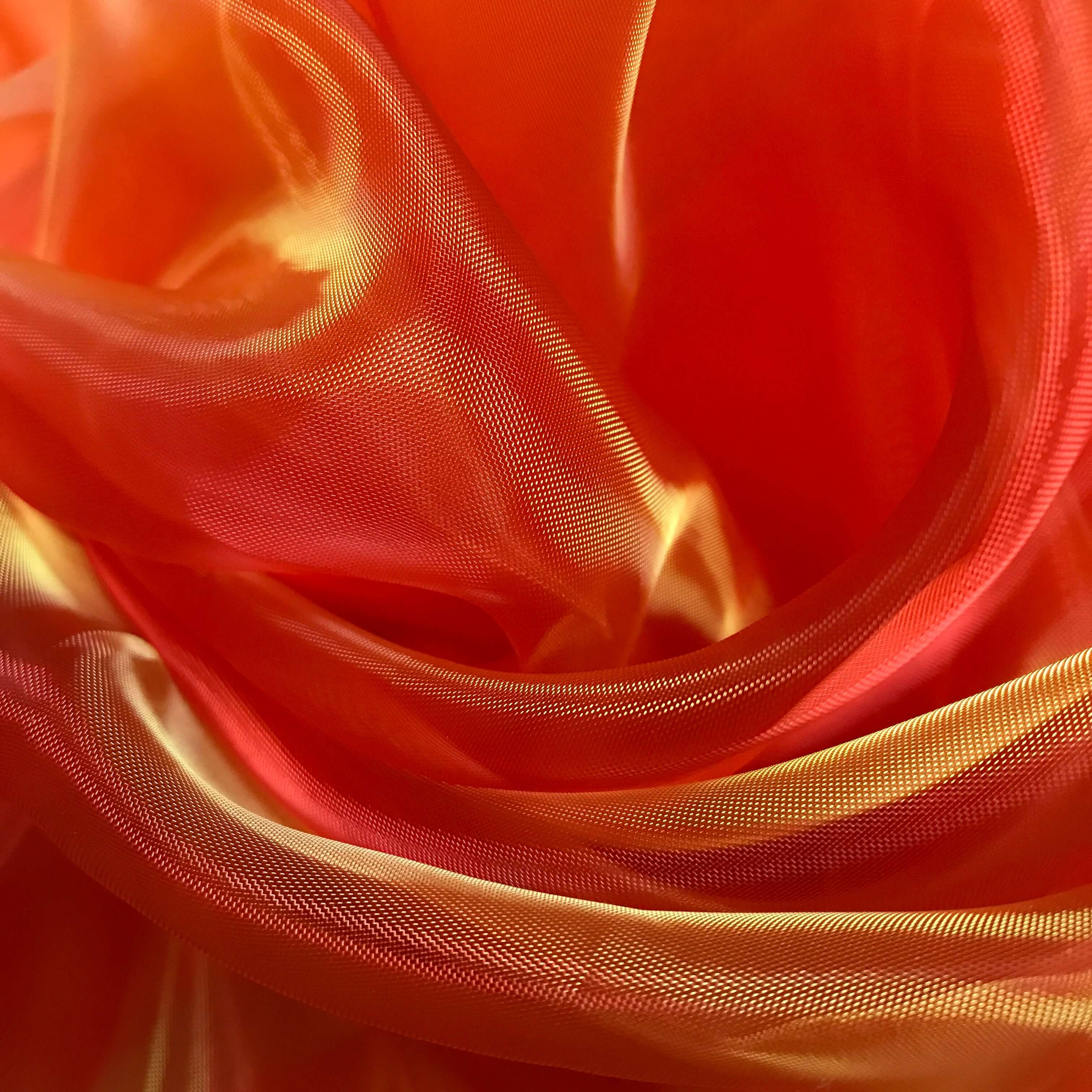 Vivid close-up of orange sheer fabric with golden yellow highlights, capturing the vibrant shimmer and flowing texture used in worship flags.