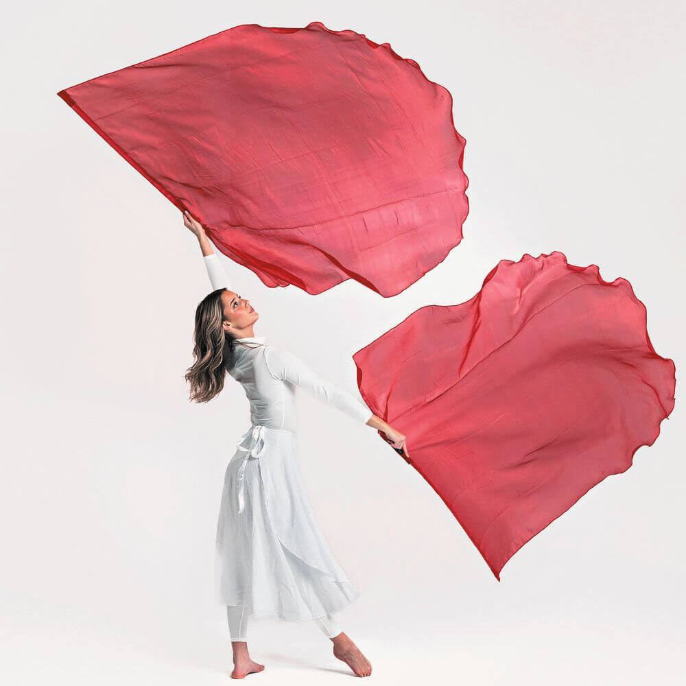 Worship dancer dressed in white lifts vibrant red flags in a powerful pose, symbolizing intercession and the blood of Jesus, set against a clean white studio background.