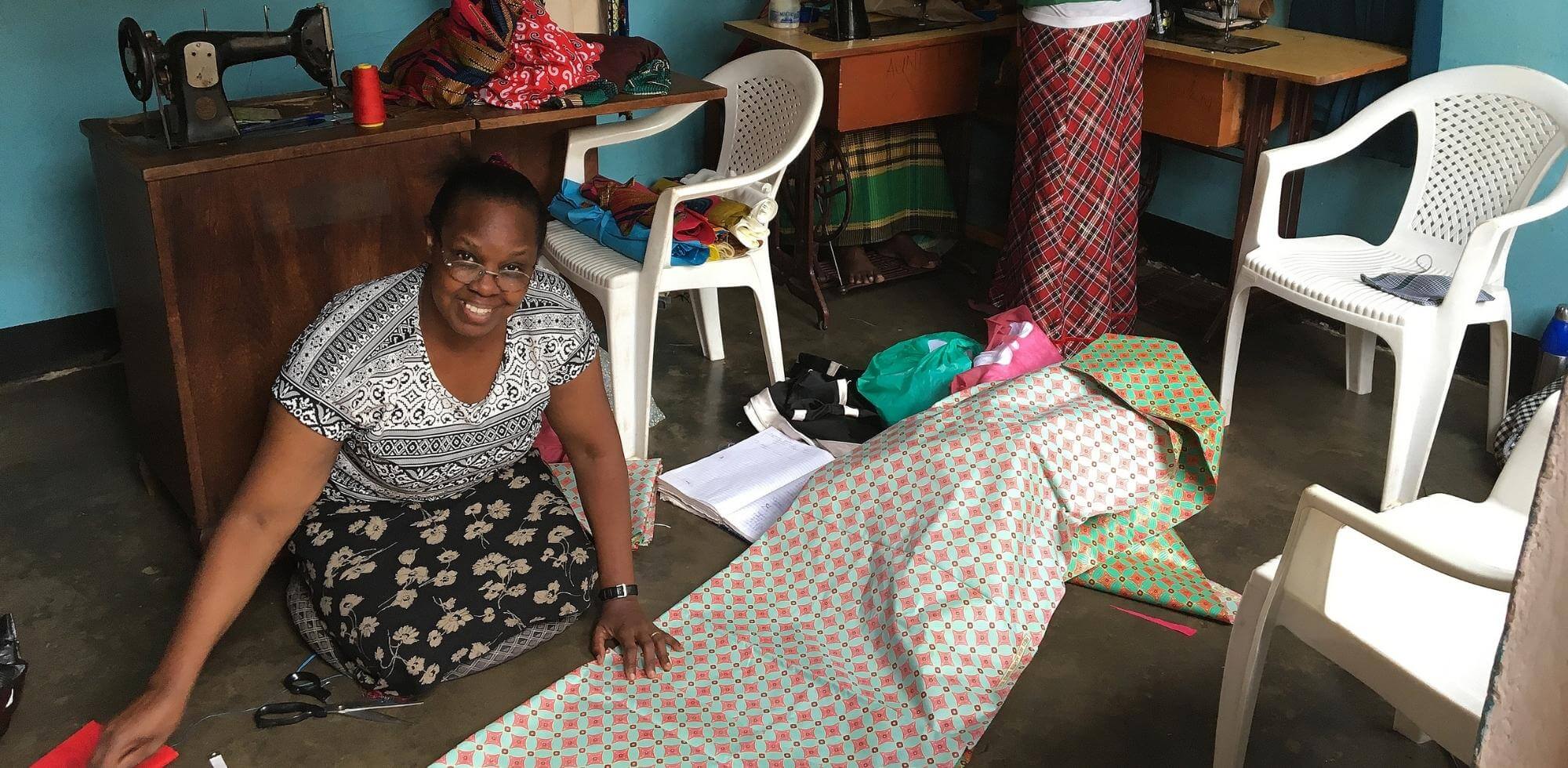 Smiling woman working with colorful fabric on the floor of a sewing room — representing joy, creativity, and empowerment through handmade craftsmanship supported by Catch the Fire Worship Flags' global impact initiatives.