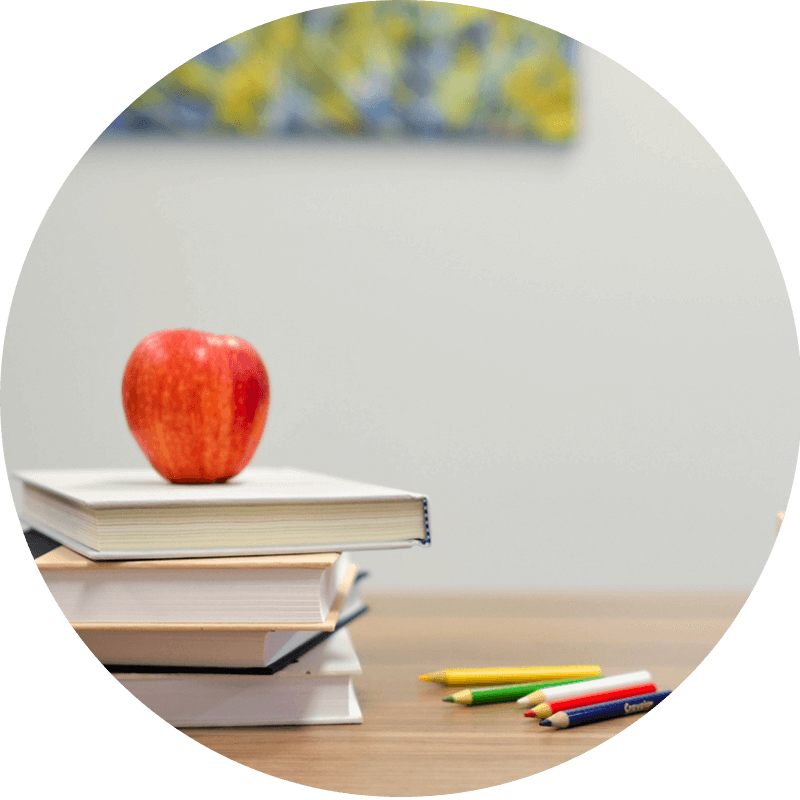 Stack of books with a red apple and colored pencils on a desk — symbolizing the foundation of learning and equipping worshippers for deeper understanding at Catch the Fire Worship Flags.