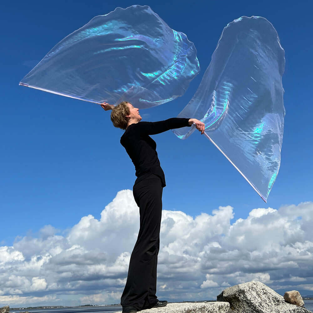Worshipper standing on a rock, lifting two large iridescent crystal worship flags under a vivid blue sky with clouds, symbolizing victory and the majesty of heaven.