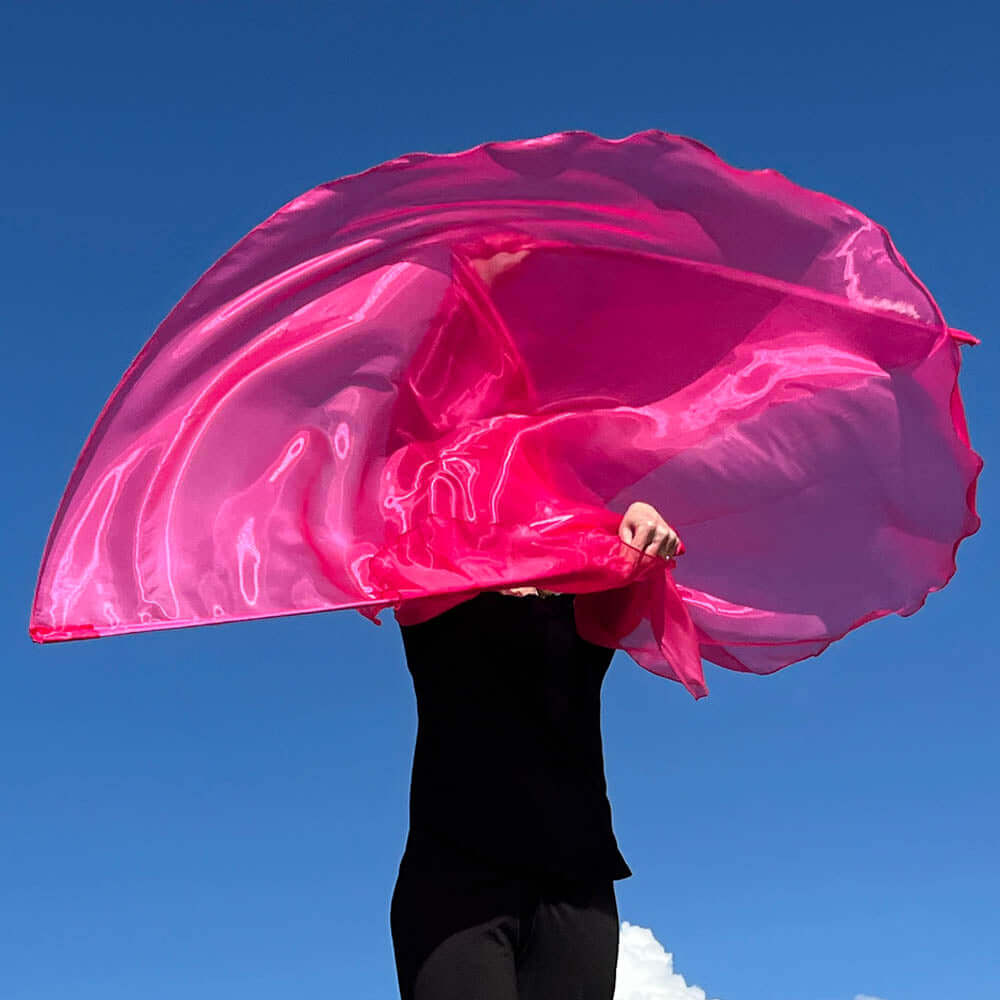 Worshipper waving a vibrant hot pink worship flag against a bright blue sky, capturing the dynamic movement and joyful expression in praise.