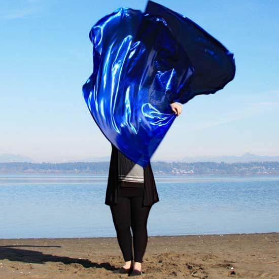 "Worshipper on a sandy beach raising deep sapphire blue worship flags with iridescent sheen, flowing in prophetic movement under a clear sky.