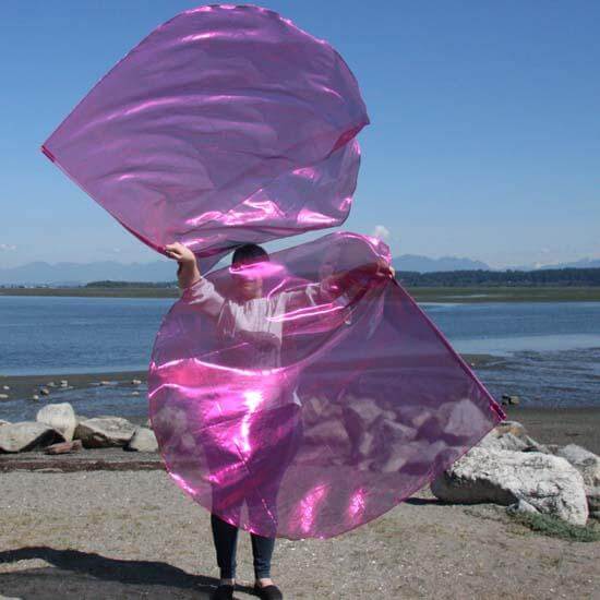 Worshipper flowing with large scarlet pink worship flags on a coastal shoreline, expressing prophetic movement and joy in praise.