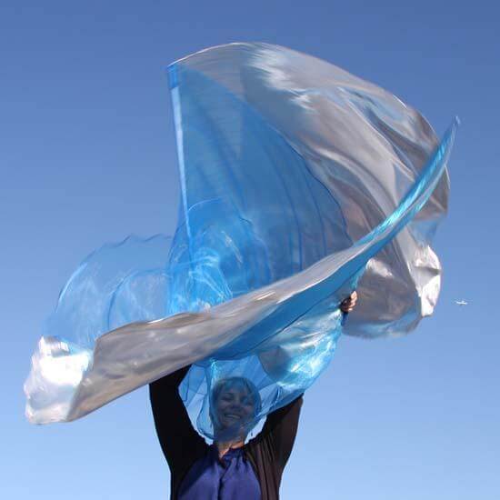 Worshipper smiling beneath billowing blue and silver praise flags against a bright sky, symbolizing freedom and joyful expression in worship.