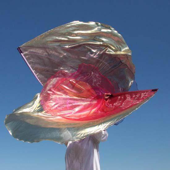 Person worshiping with large multi-layer worship flags in scarlet, purple, and gold tones, flowing dynamically against a clear blue sky during a flagging movement.