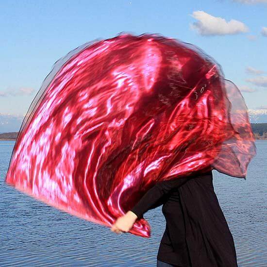 Worship dancer holding a billowing scarlet and wine red metallic worship flag beside a calm waterfront, capturing movement, reflection, and passionate praise.