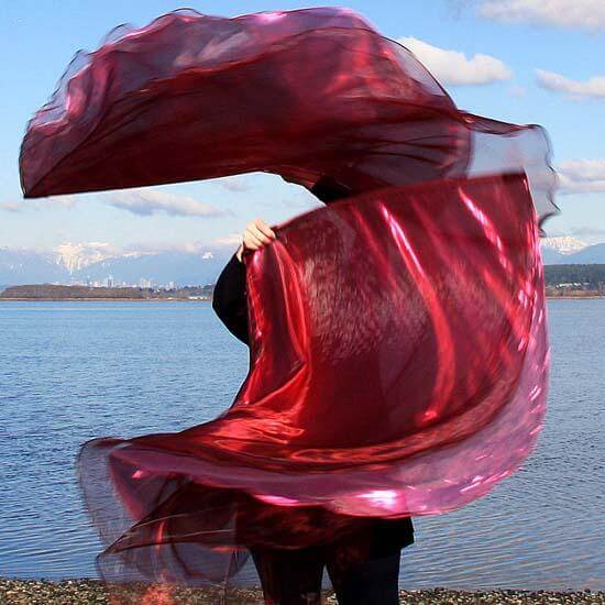 Worship dancer gracefully sweeping layered wine and scarlet red flags by the water's edge, mountains in the background, symbolizing intercessory worship and the healing power of God's presence.