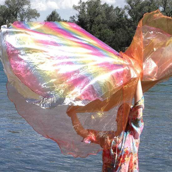 Dancing with multi-layered shimmering worship flags, flowing in vibrant colors by the water, celebrating faith.