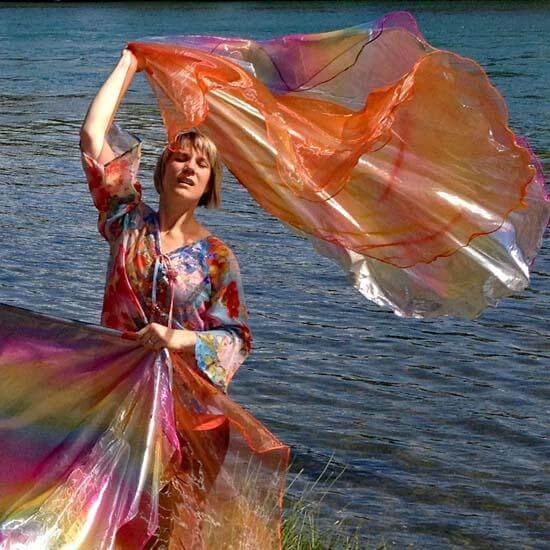 Dancer joyfully flowing with colorful worship flags by the water, embodying praise and intercession with shimmering glory.