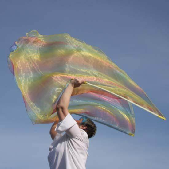 Worshipper lifts a single iridescent yellow and rainbow flag high into the sky under soft sunlight, with movement captured against a clear blue background.