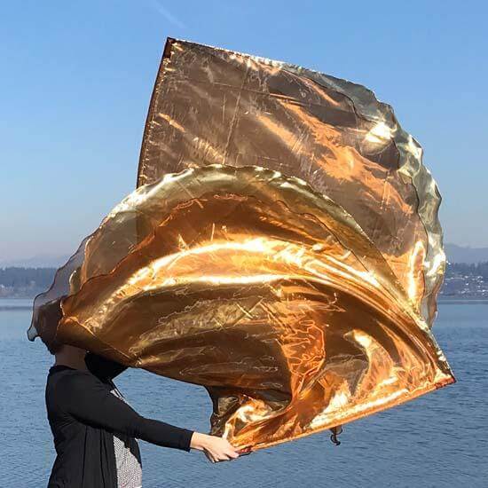 Worshipper lifts flowing bronze and gold flags against a lake backdrop with blue skies.
