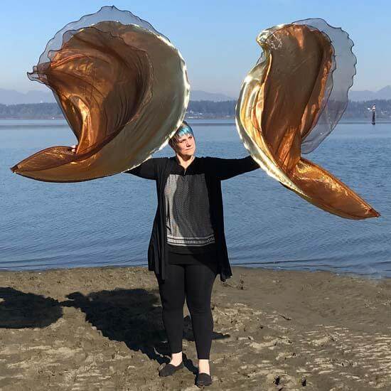 Woman worshipping with flowing bronze and gold worship flags near the water.