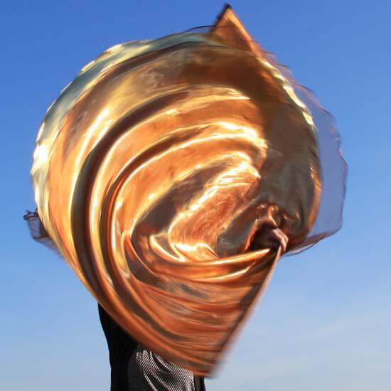 A large bronze and gold worship flag swirling mid-air, held by a person under a blue sky.