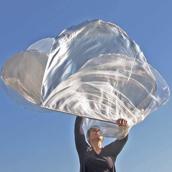 Woman lifts crystal and silver worship flags in worship under a blue sky, symbolizing purity and the glory of God's presence.