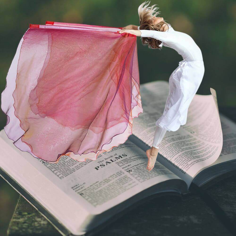 Worship dancer holding a pink worship flag above an open Bible turned to the Book of Psalms, symbolizing scriptural praise through movement.