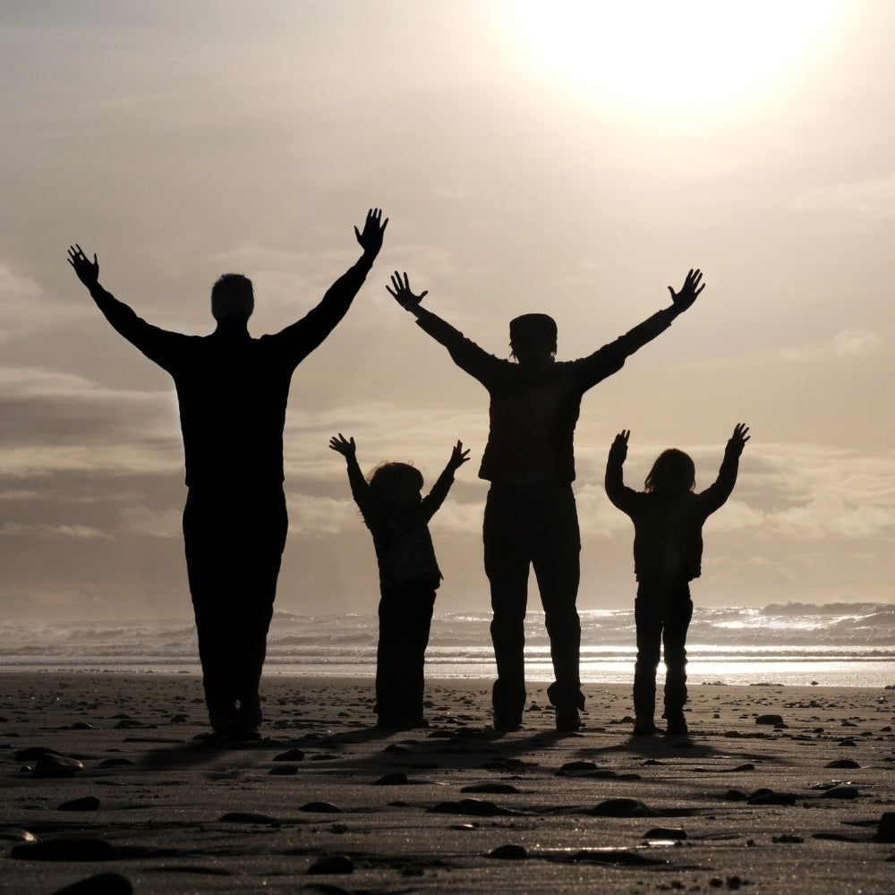 Silhouetted family lifting hands in worship at sunset on the beach, representing generational praise and raising children in faith.