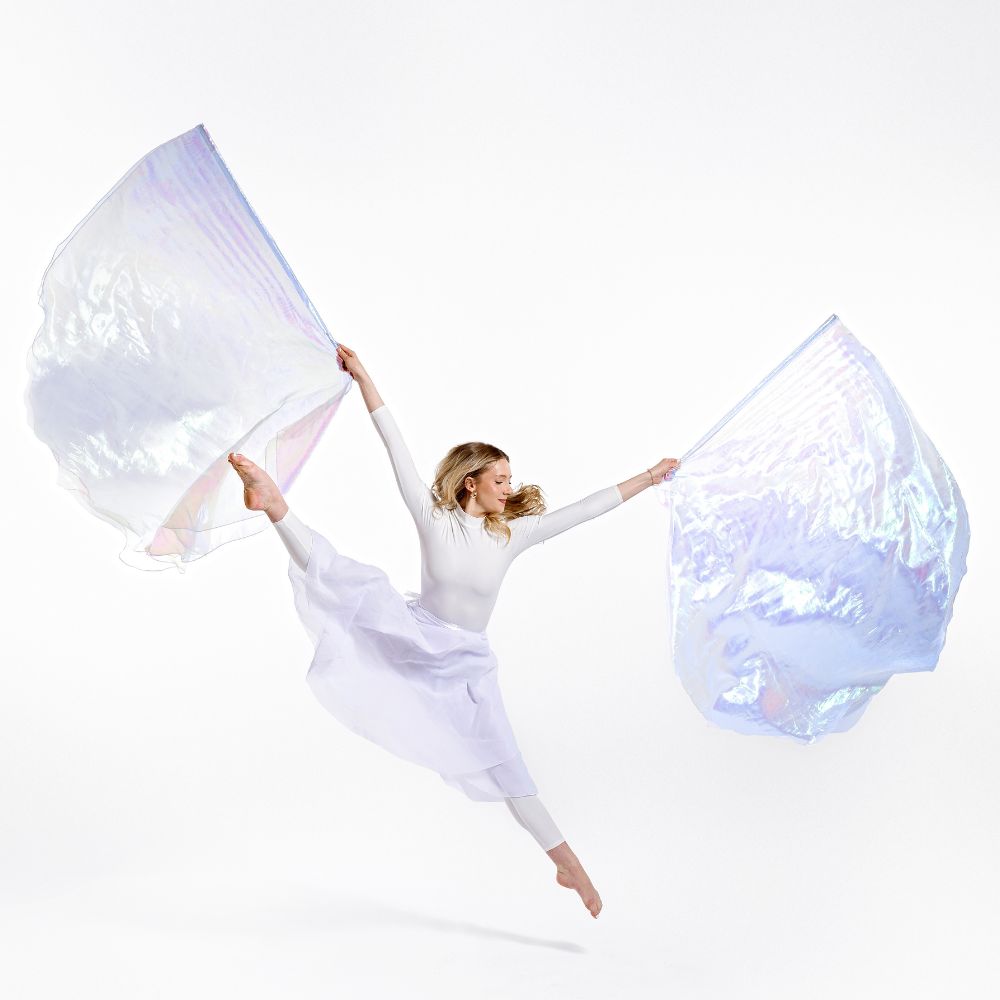 Worship dancer leaps with holy & blameless iridescent double-layer worship flags. Flags represent purity, the Bride of Christ, and spiritual victory in movement.