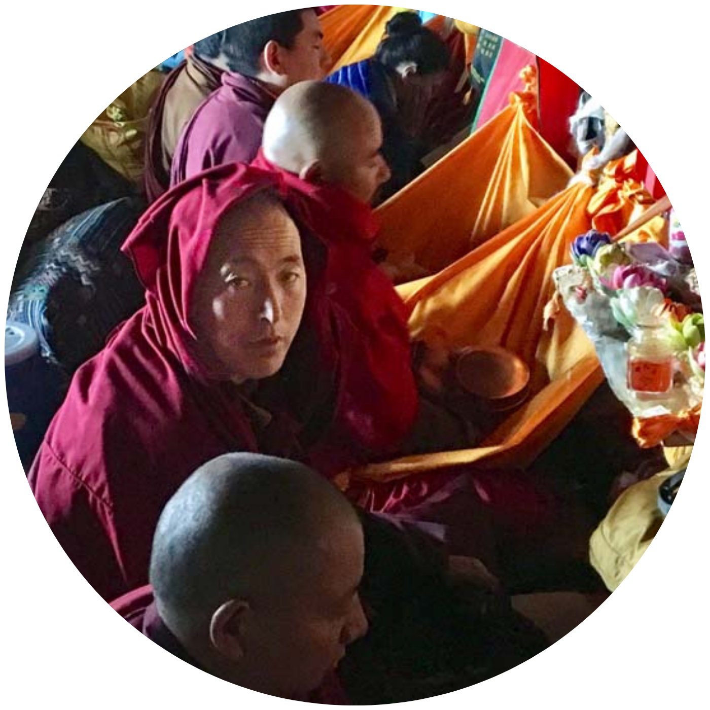 Monks in deep red robes participating in a traditional Bhutanese ceremony with vibrant orange textiles and ceremonial items
