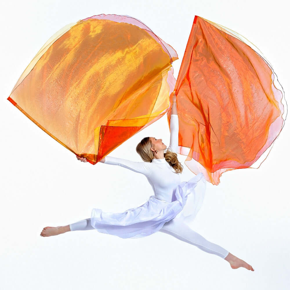Prophetic dancer leaps with Fan Into Flame triple-layer flags in red, orange, and yellow. A vibrant expression of stirring the gift of God into action.