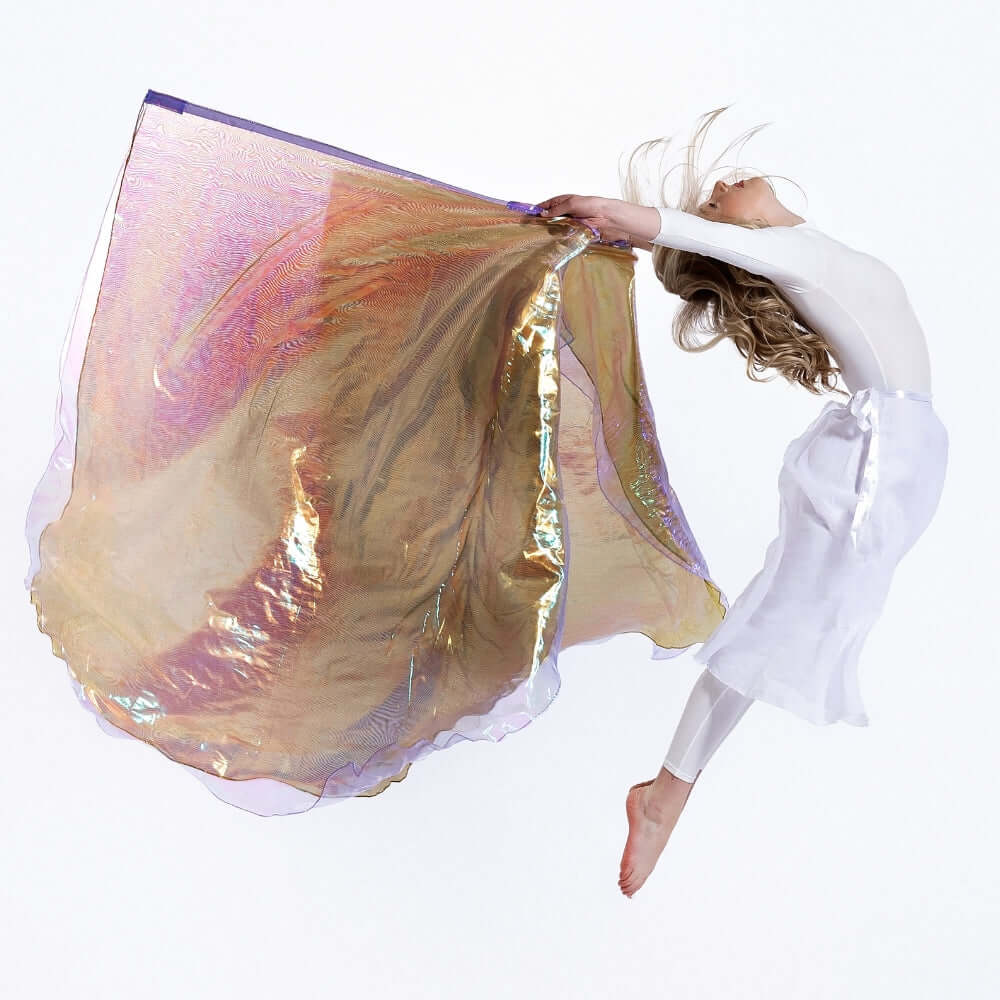 Christian dancer jumps midair with Harp & Bowl worship flags, showcasing layered gold, crystal and lilac iridescence – worship dance flags with biblical color meaning