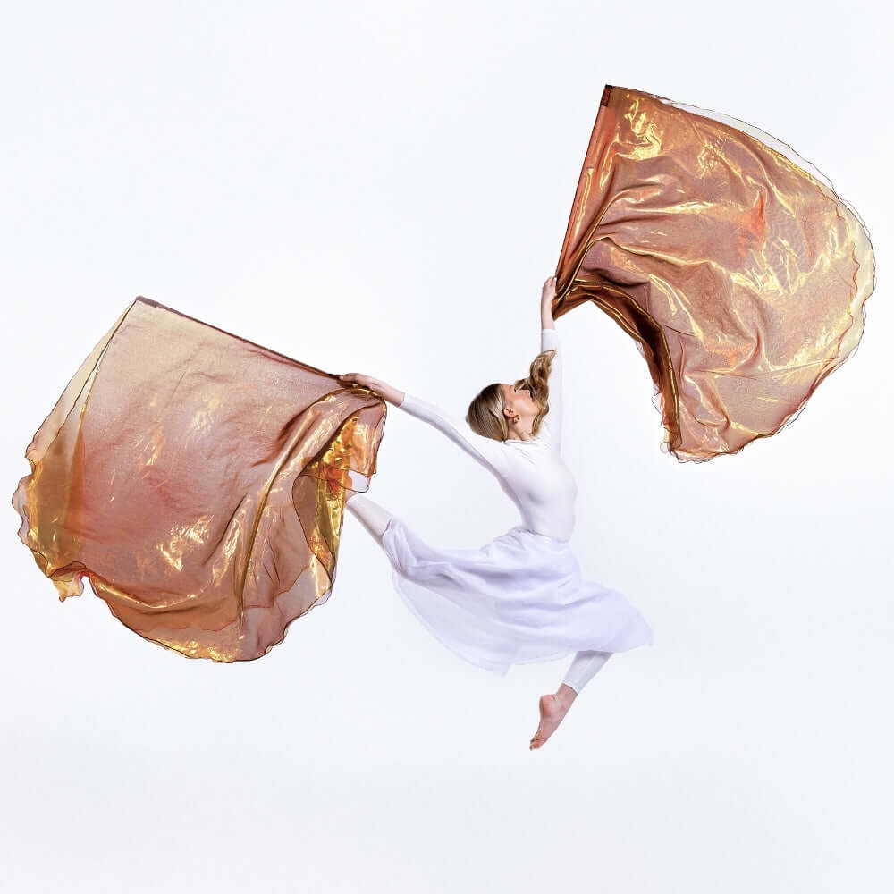 Worship dancer leaps with Jehovah Sabaoth triple-layer worship flags in bronze, gold, and coral—prophetic dance flags for strength and great for intercession and spiritual warfare.