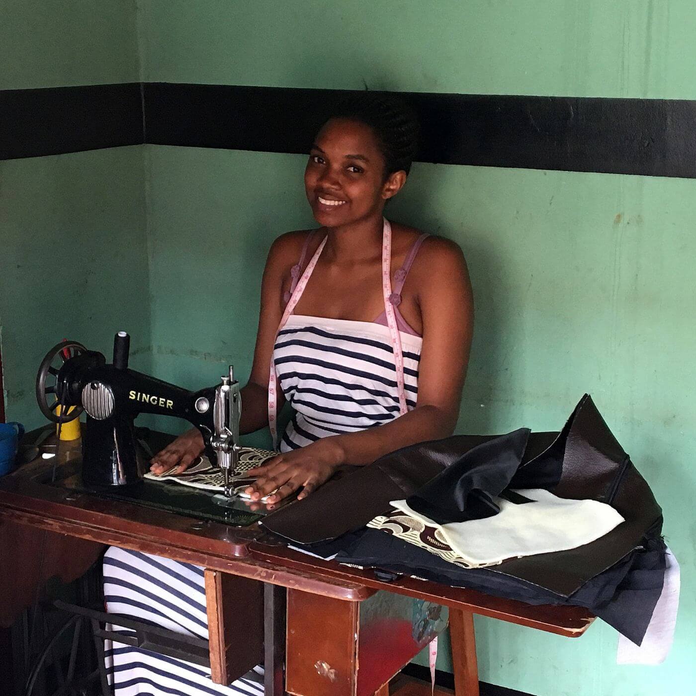 Young woman sewing with a vintage Singer machine, smiling with purpose — representing skill development, empowerment, and dignity through Catch the Fire Worship Flags’ global outreach to train women in sustainable craftsmanship.