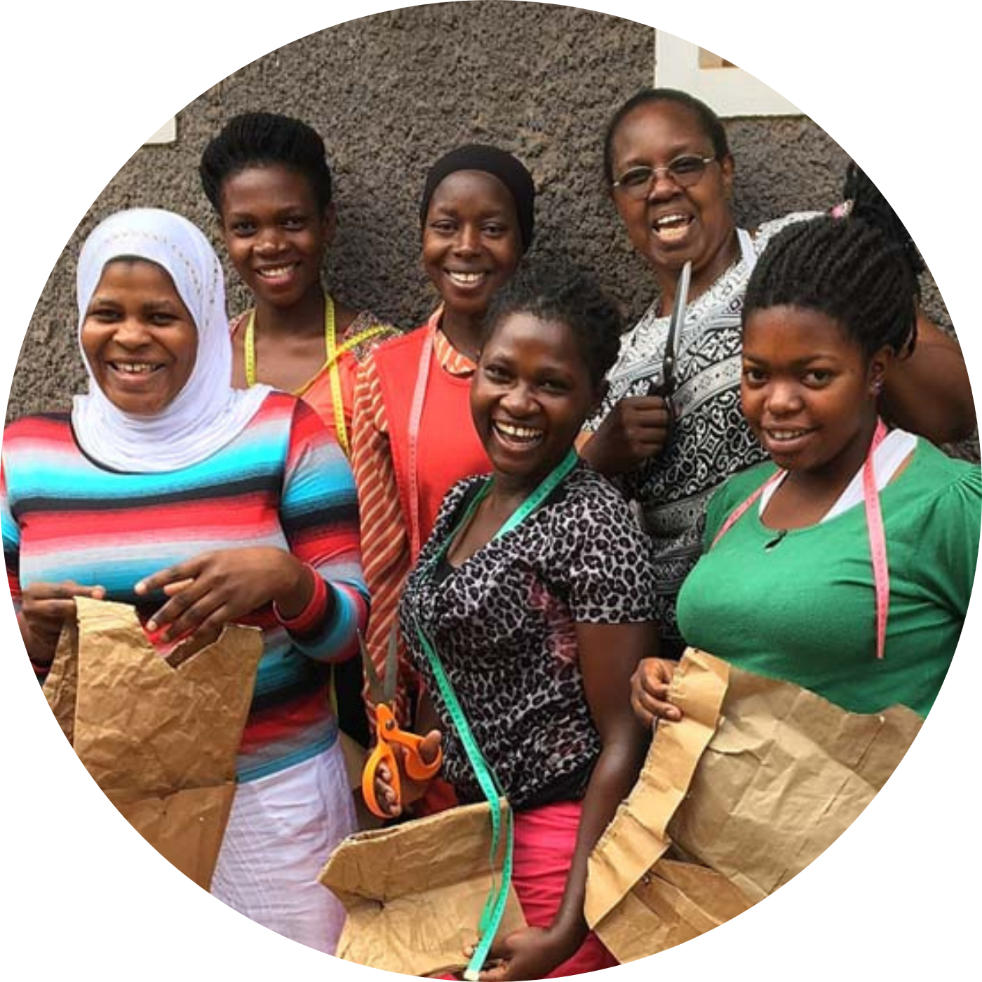 Group of smiling women in Uganda holding sewing patterns and scissors in a tailoring training session