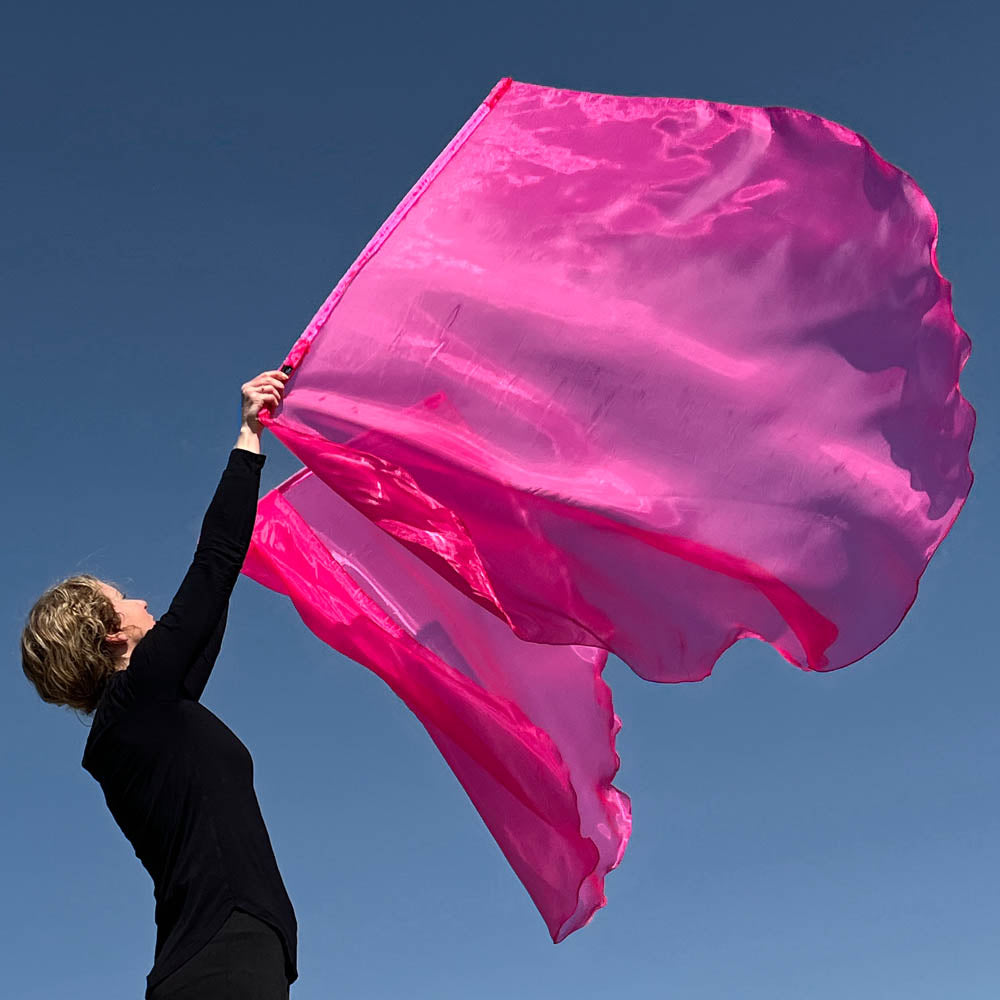 Female praise dancer worshipping outdoors with large scarlet pink shimmer worship flags flowing against a clear blue sky; flags are lightweight and mounted on flexible rods.