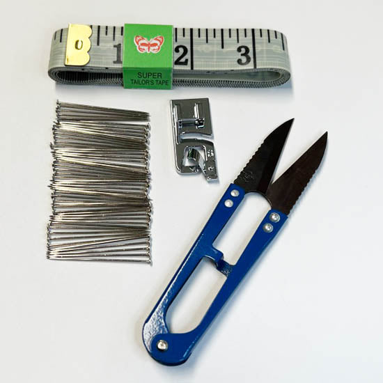 DIY worship flag sewing kit with measuring tape, dressmaker pins, universal rolled hem presser foot, and blue sewing scissors on white background.